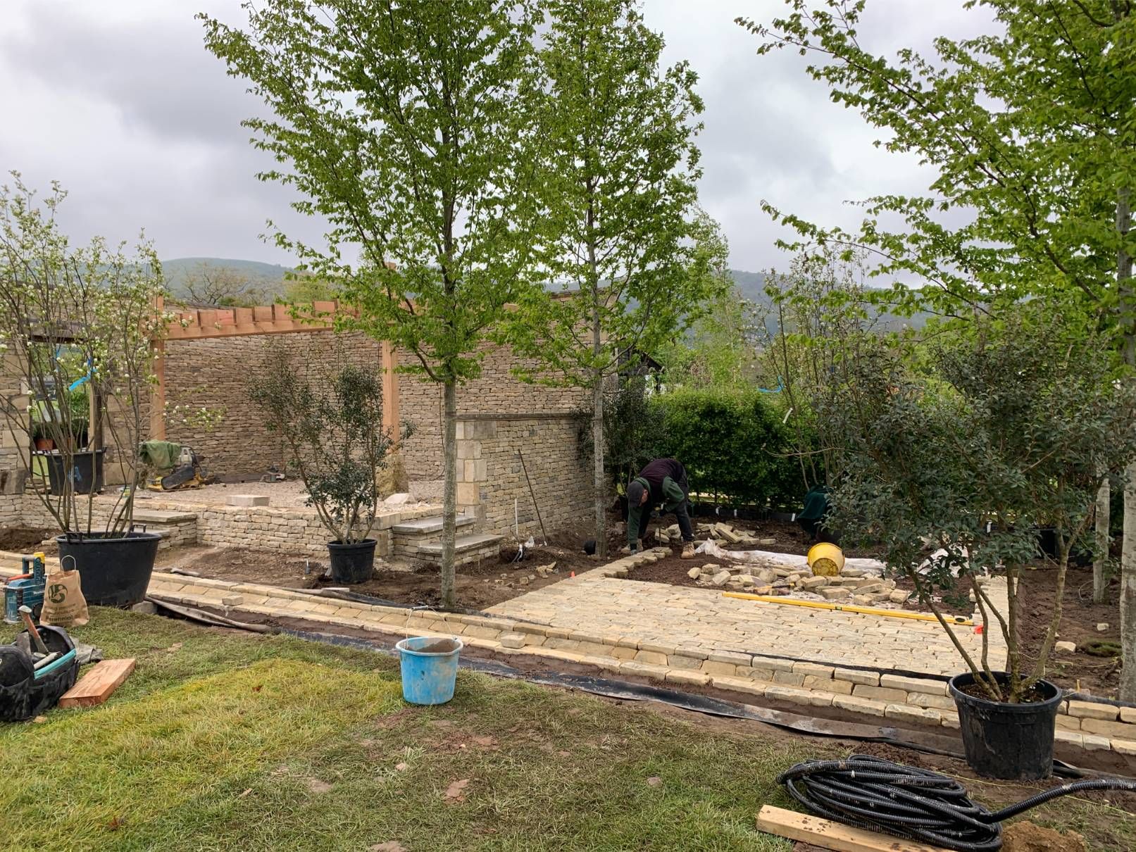 Garden landscaping underway with green trees and cloudy sky.