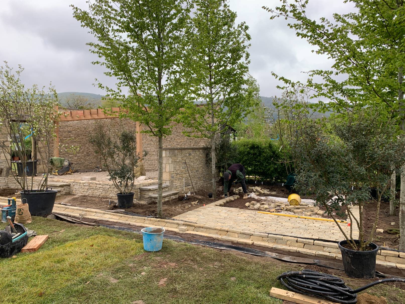 Garden landscaping underway with green trees and cloudy sky.